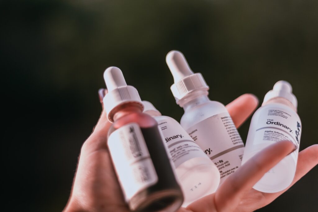 A hand holding four bottles of serum from the brand The Ordinary.